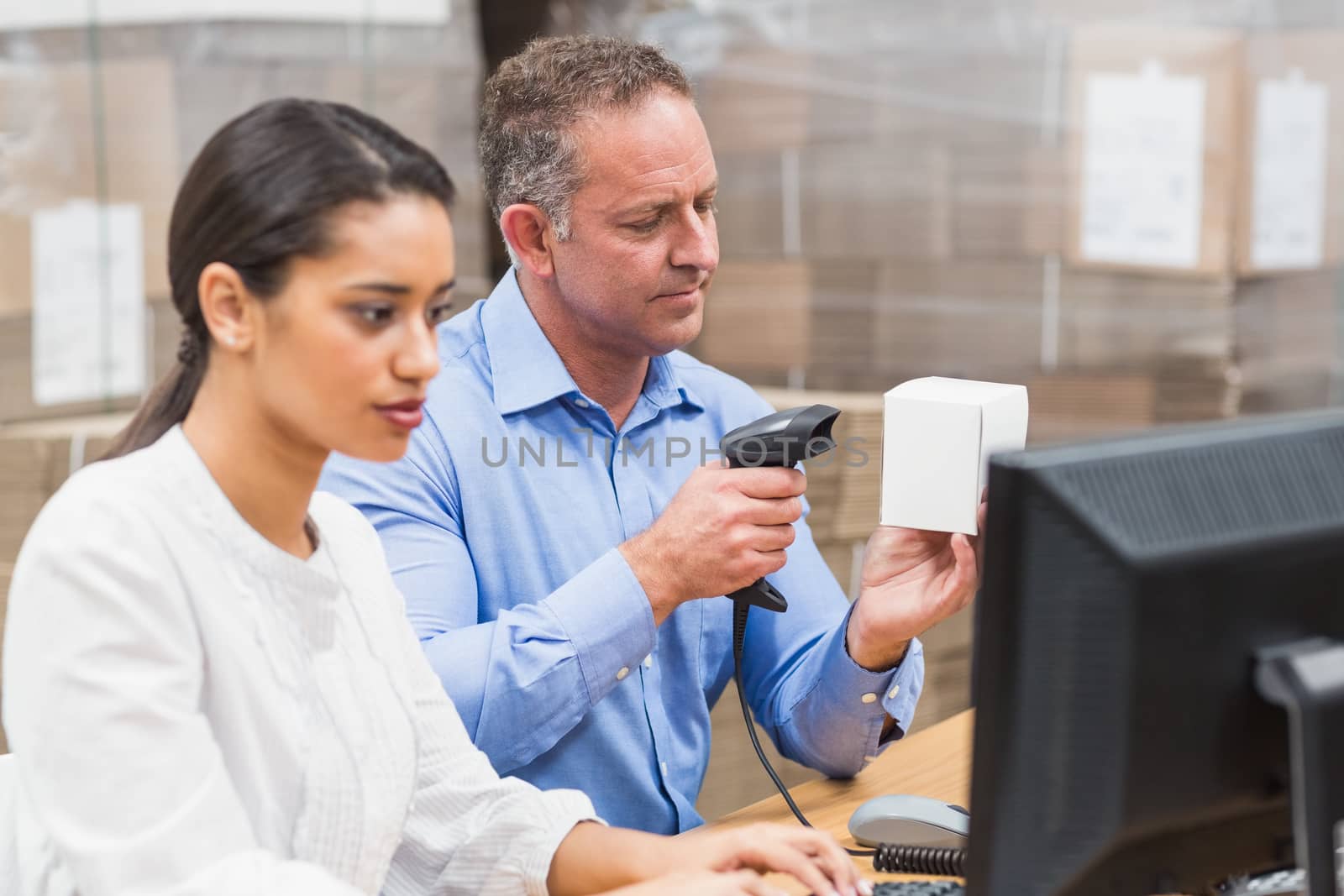 Manager scanning box while his colleague typing on laptop by Wavebreakmedia