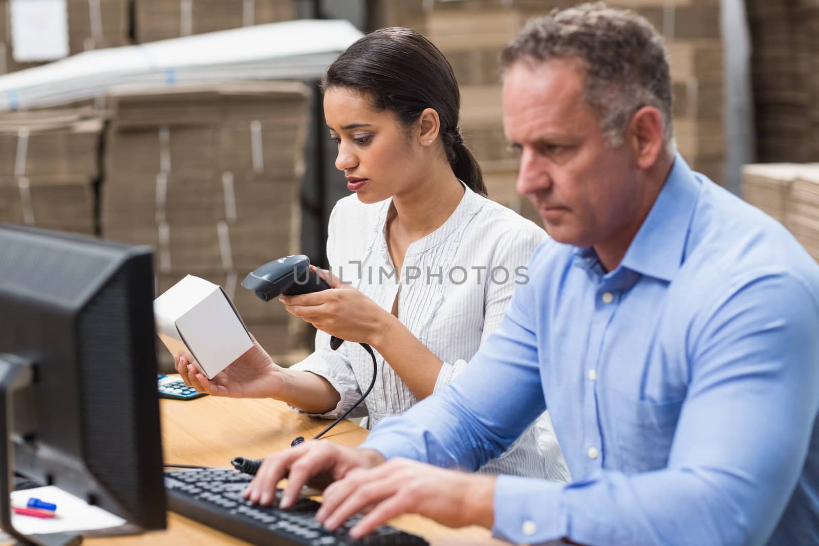Manager scanning box while her colleague typing on laptop in a large warehouse