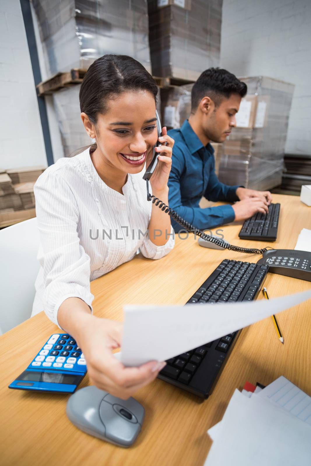 Manager making a phone call while reading a document in a large warehouse