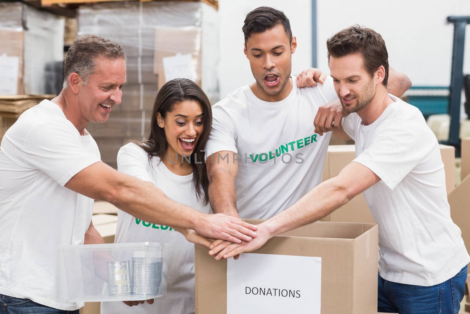 Volunteer team holding hands on a box of donations in a large warehouse