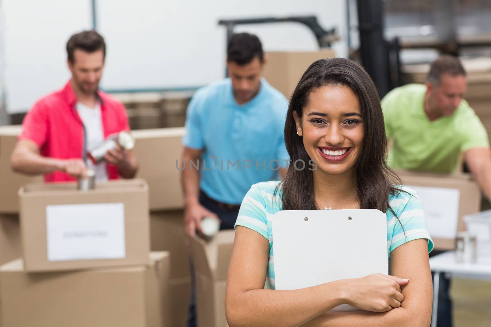 Smiling young female volunteer holding clipboard in a large warehouse