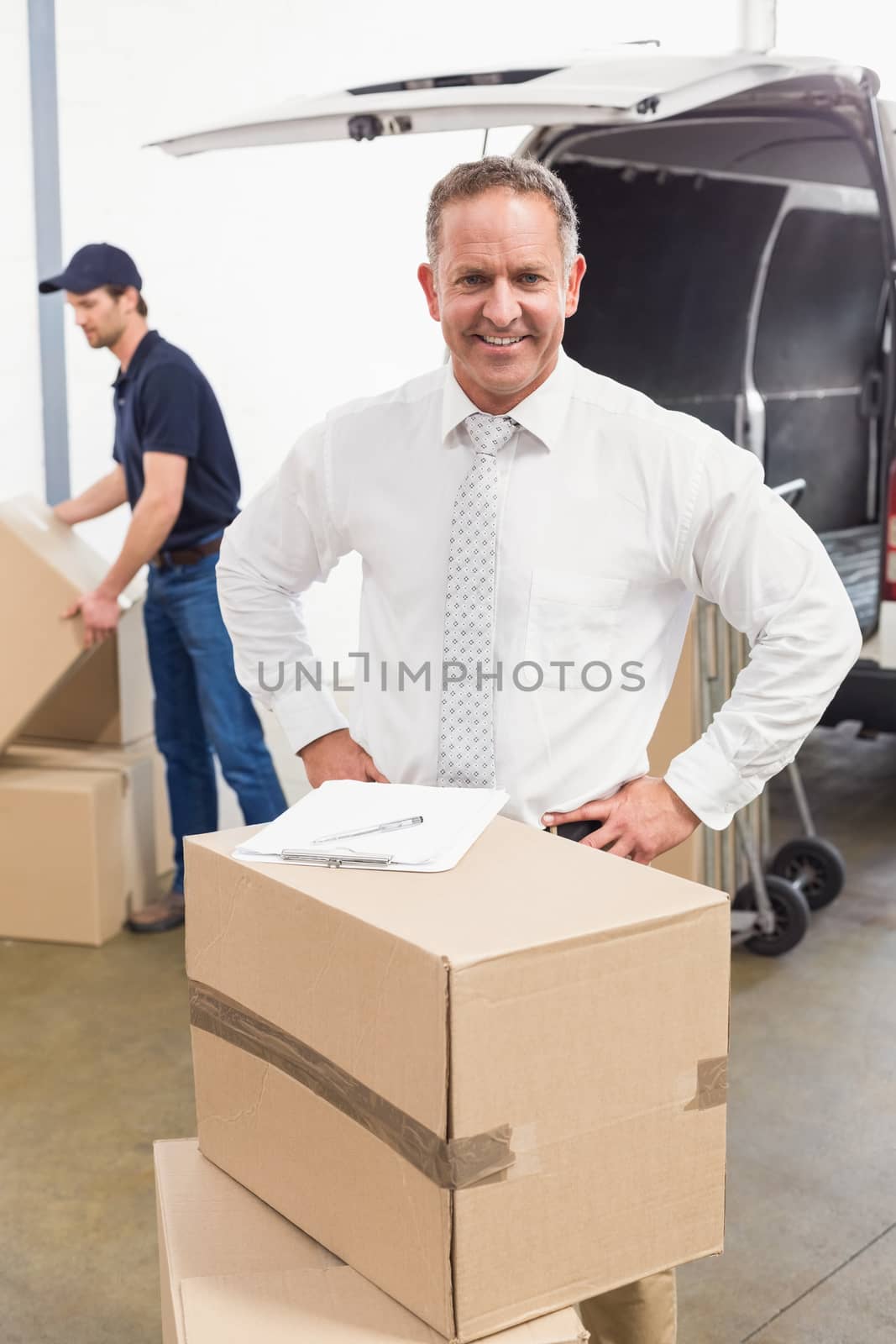 Smiling manager standing behind stack of cardboard boxes by Wavebreakmedia