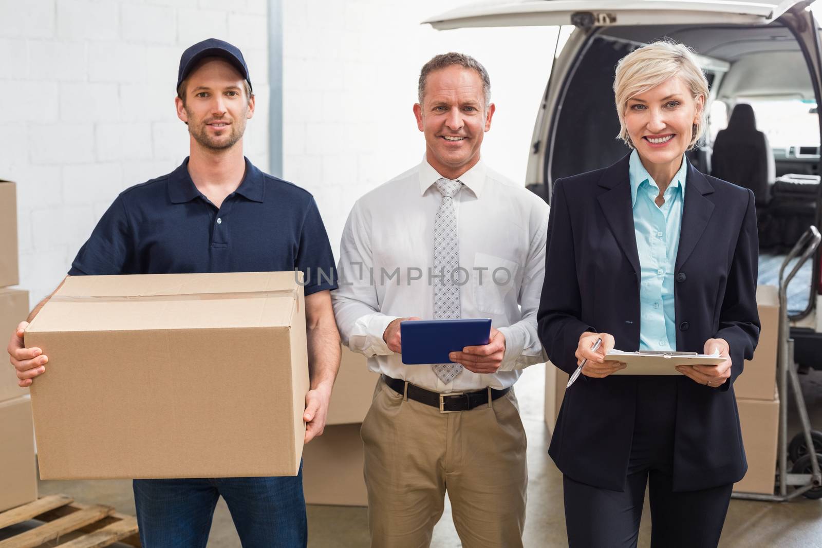 Warehouse managers and delivery driver smiling at camera in a large warehouse