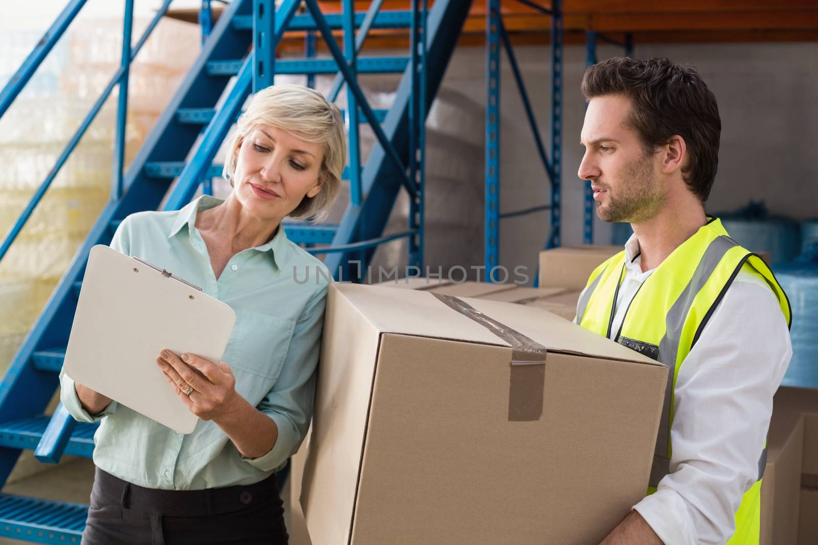Warehouse manager and worker looking at clipboard in a large warehouse