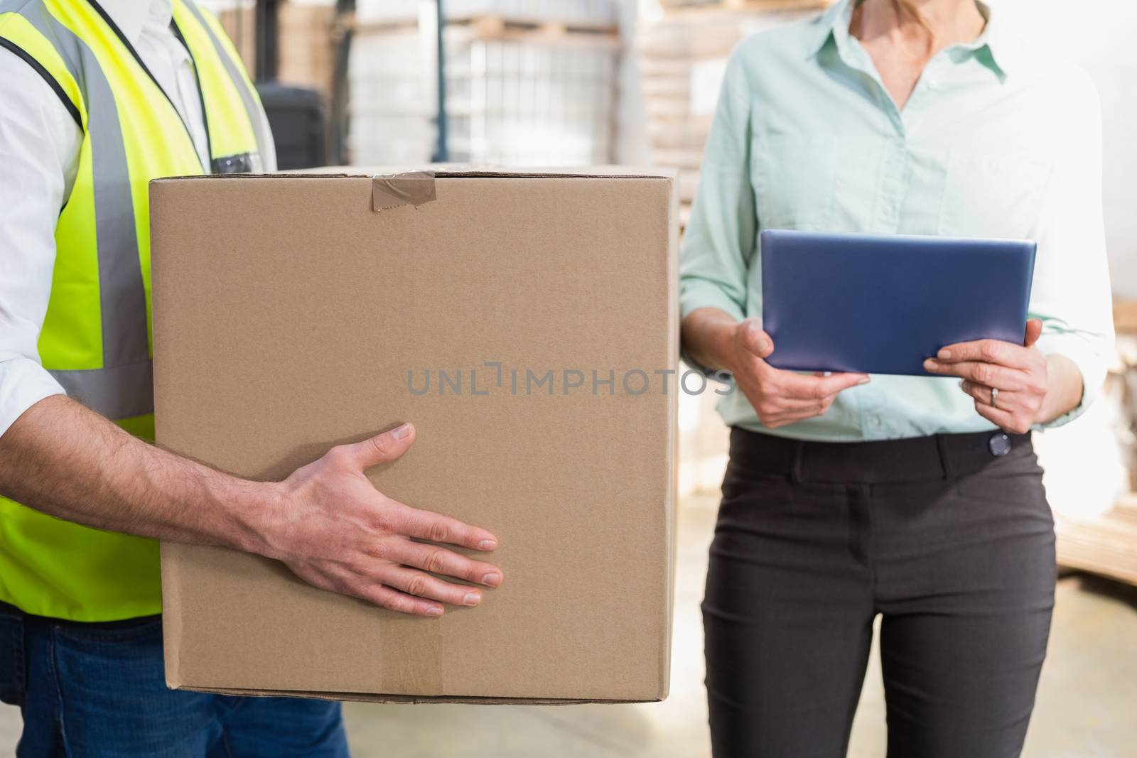 Worker carrying box with manager holding tablet pc in a large warehouse