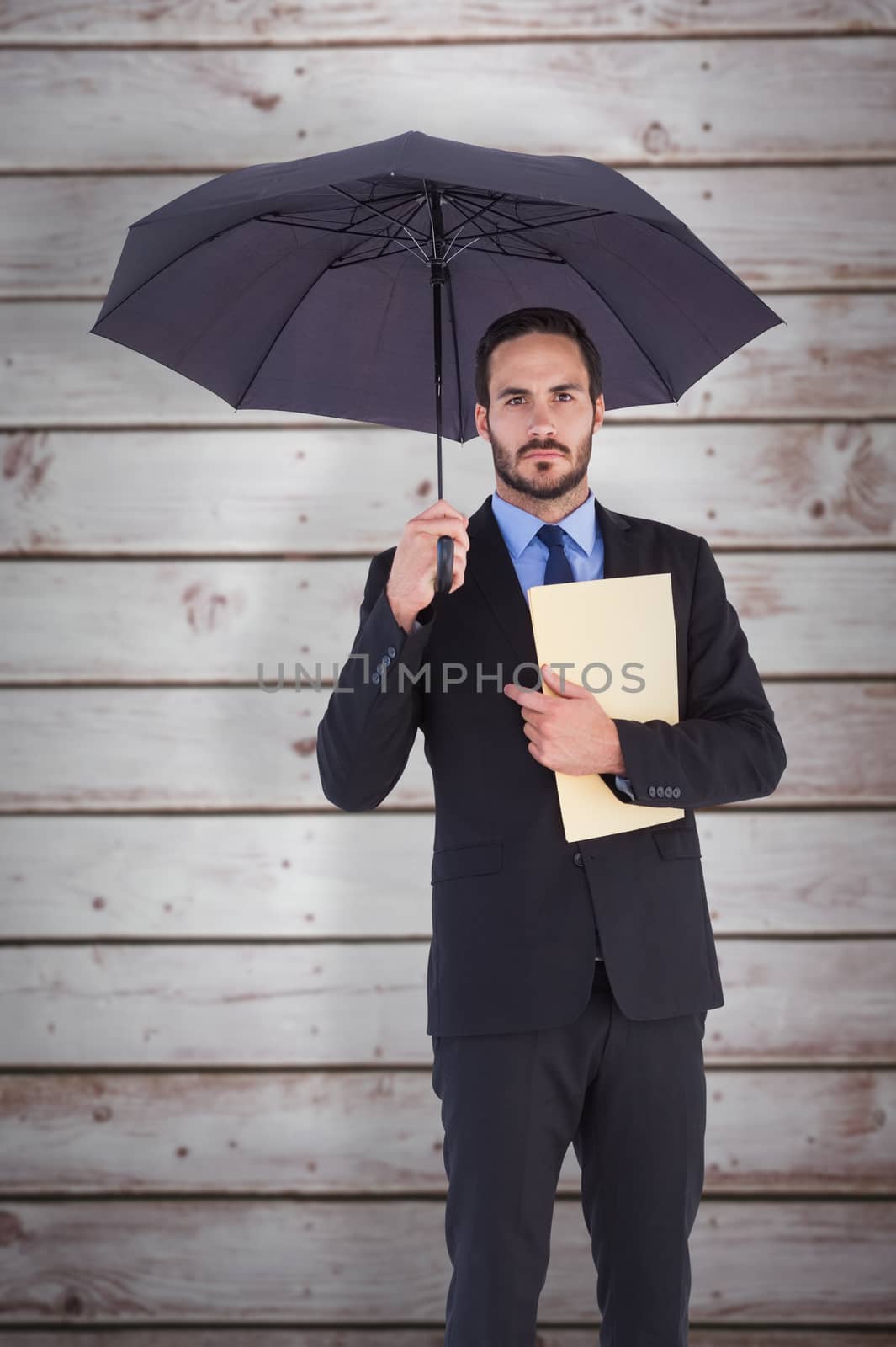 Serious businessman holding a file under umbrella against wooden planks