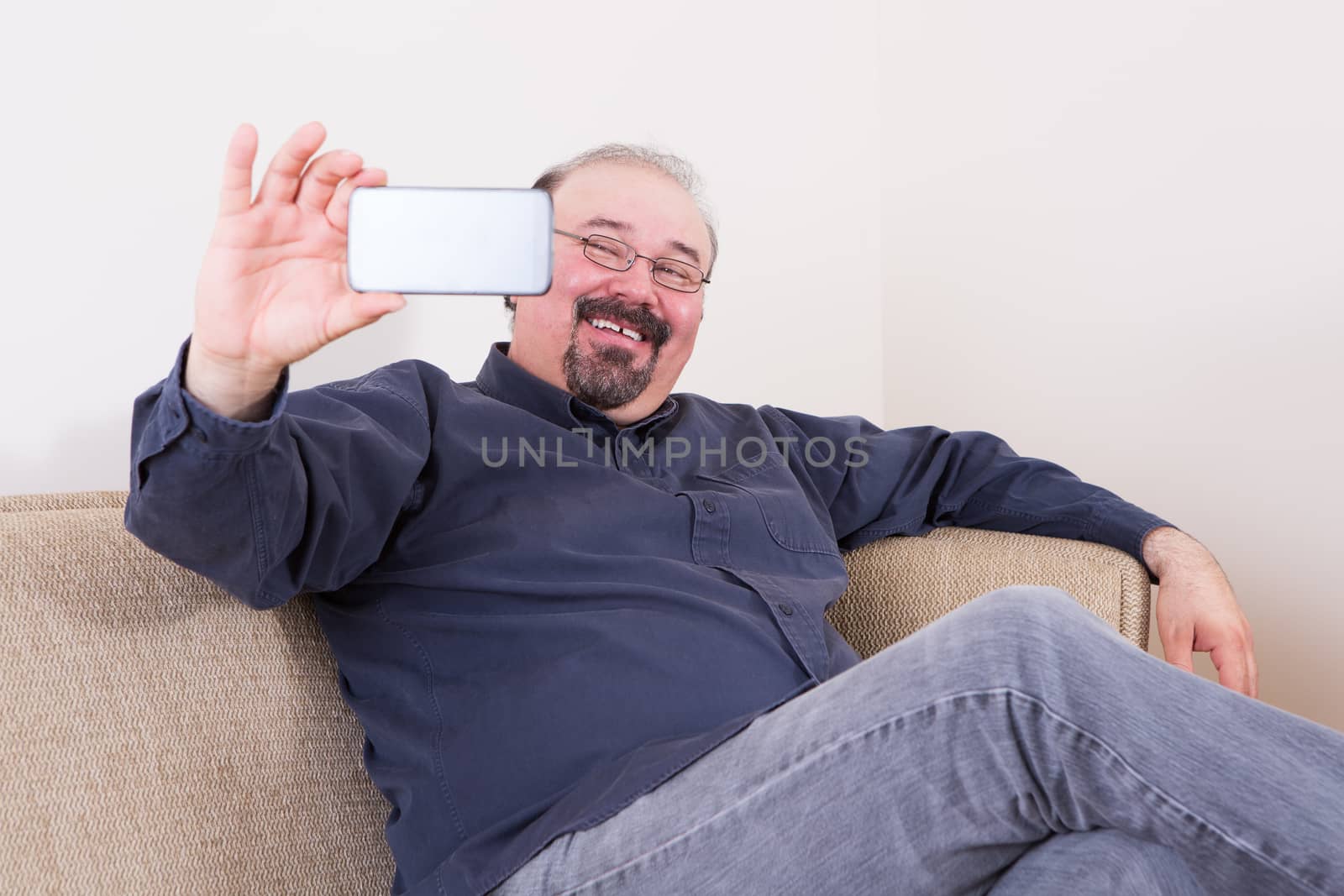 Happy man taking a selfie for his friends on the social media on his smartphone posing on a couch at home looking at the camera with a beaming smile