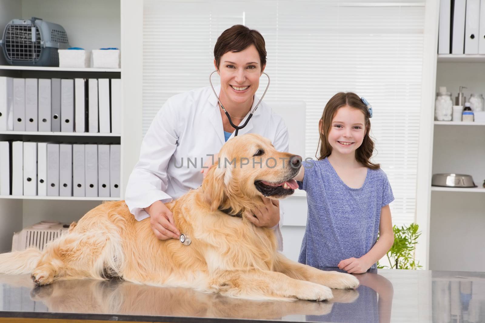Smiling vet examining a dog with its owner in medical office