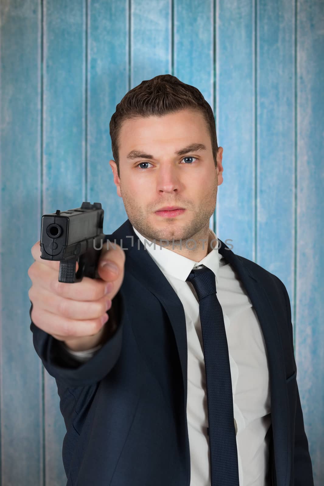 Serious businessman pointing a gun against wooden planks