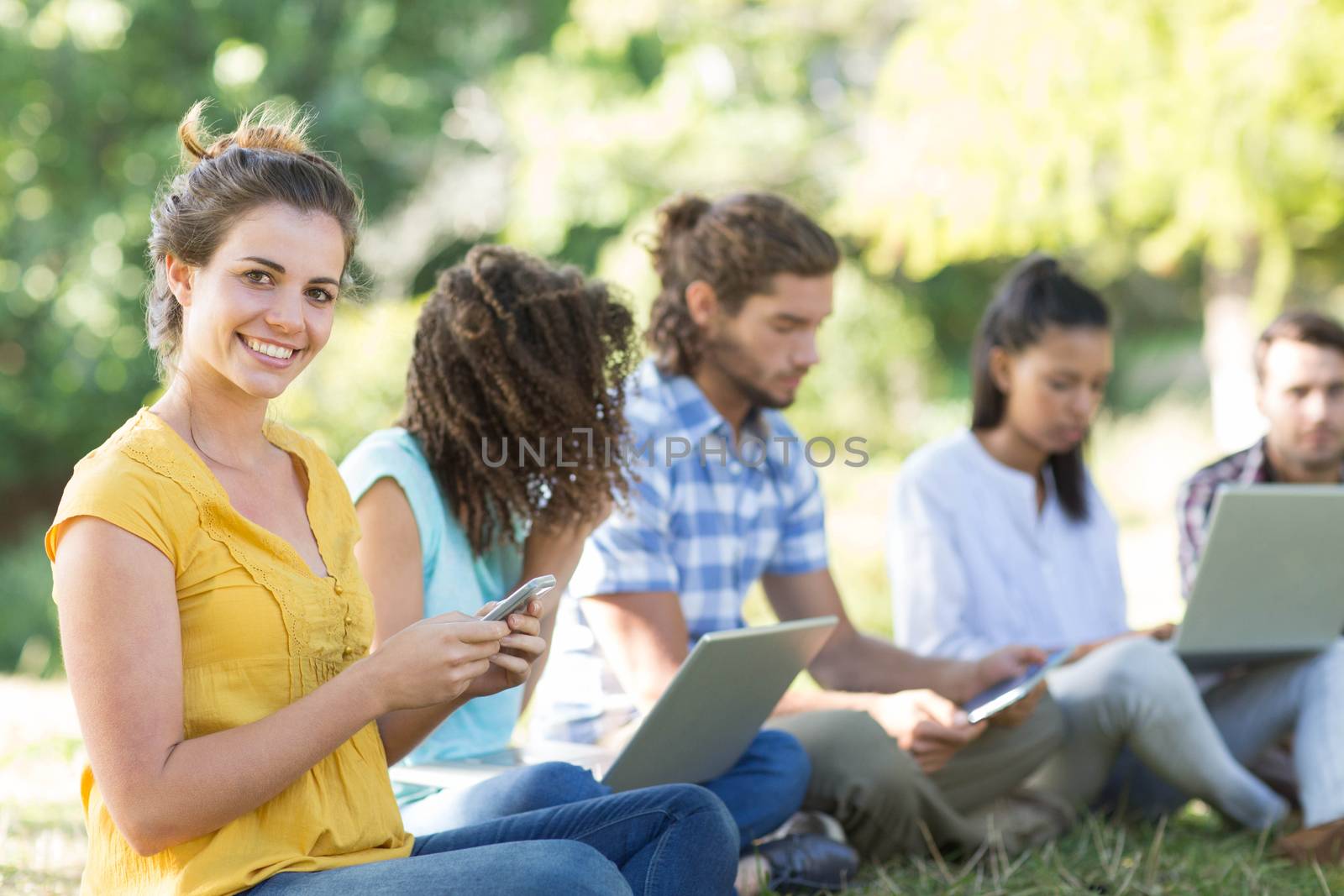 Smiling friends using media devices in park on a sunny day