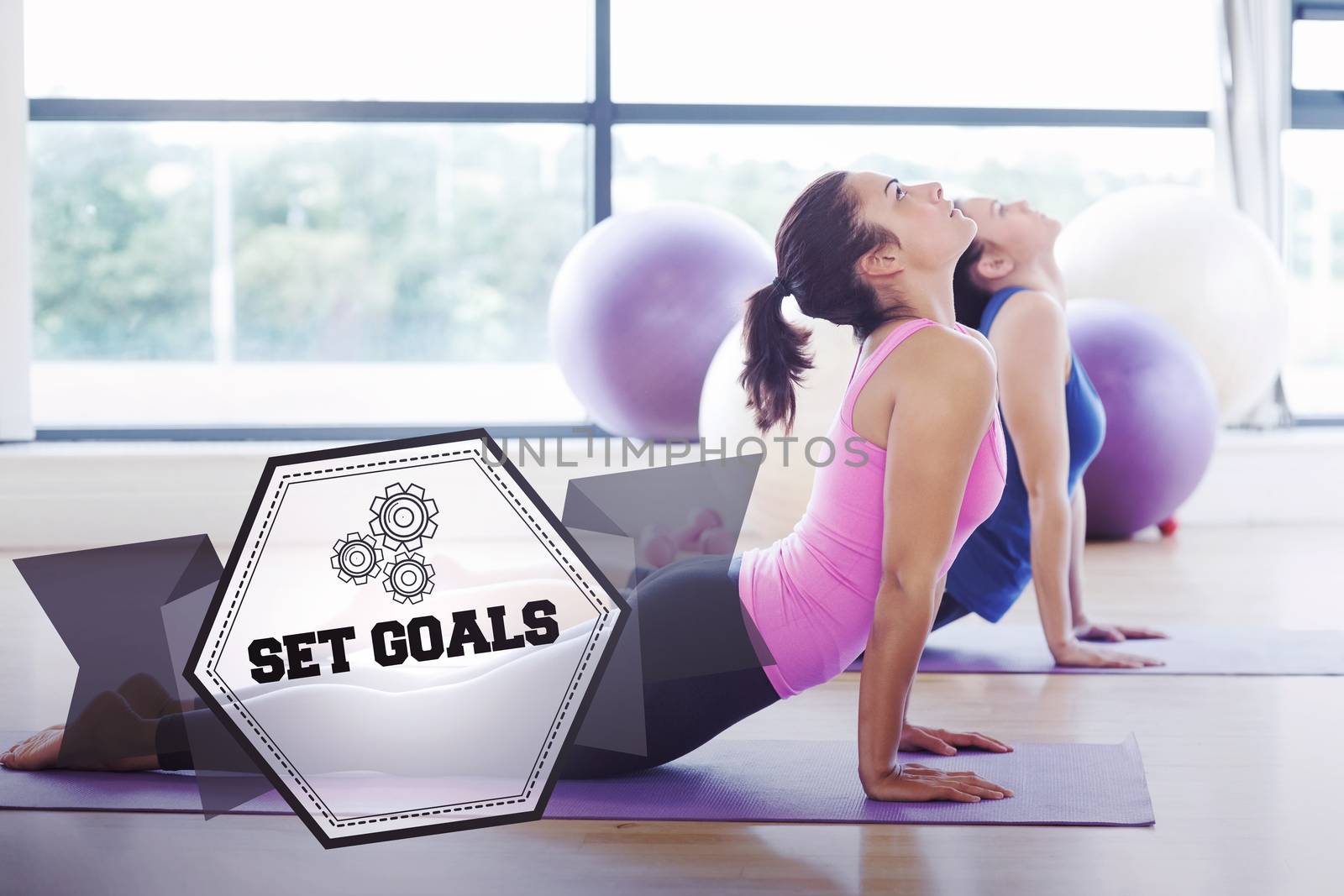 The word set goals and fit women doing the cobra pose in fitness studio against hexagon