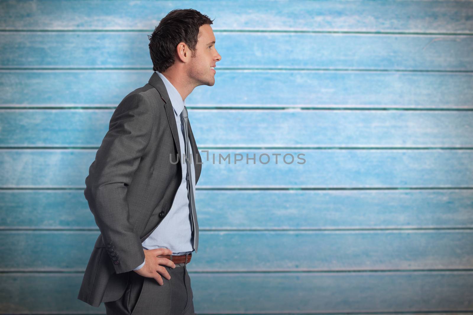 Smiling businessman with hands on hips against wooden planks