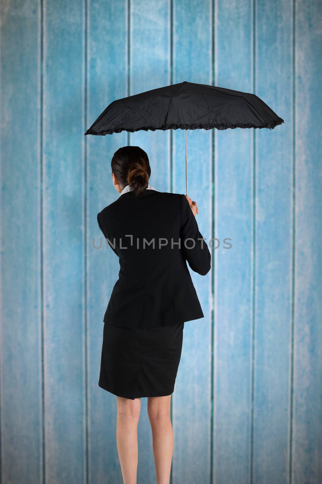 Young businesswoman holding umbrella against wooden planks