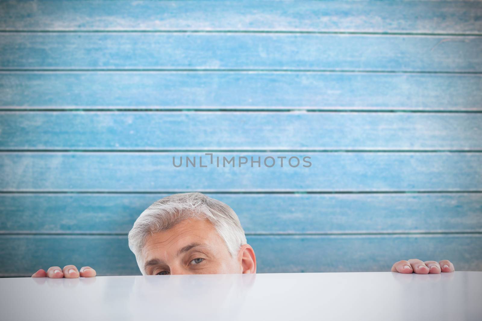 Composite image of businessman peeking over desk by Wavebreakmedia