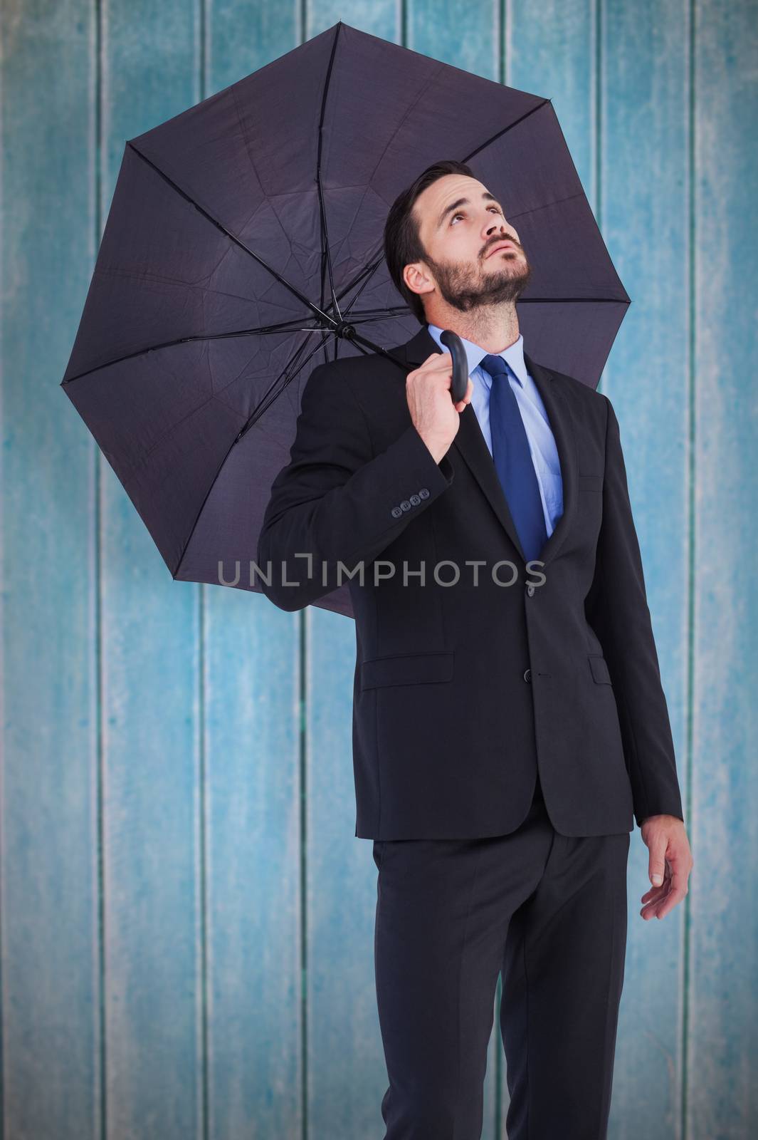 Businesswoman in suit holding umbrella while looking up against wooden planks