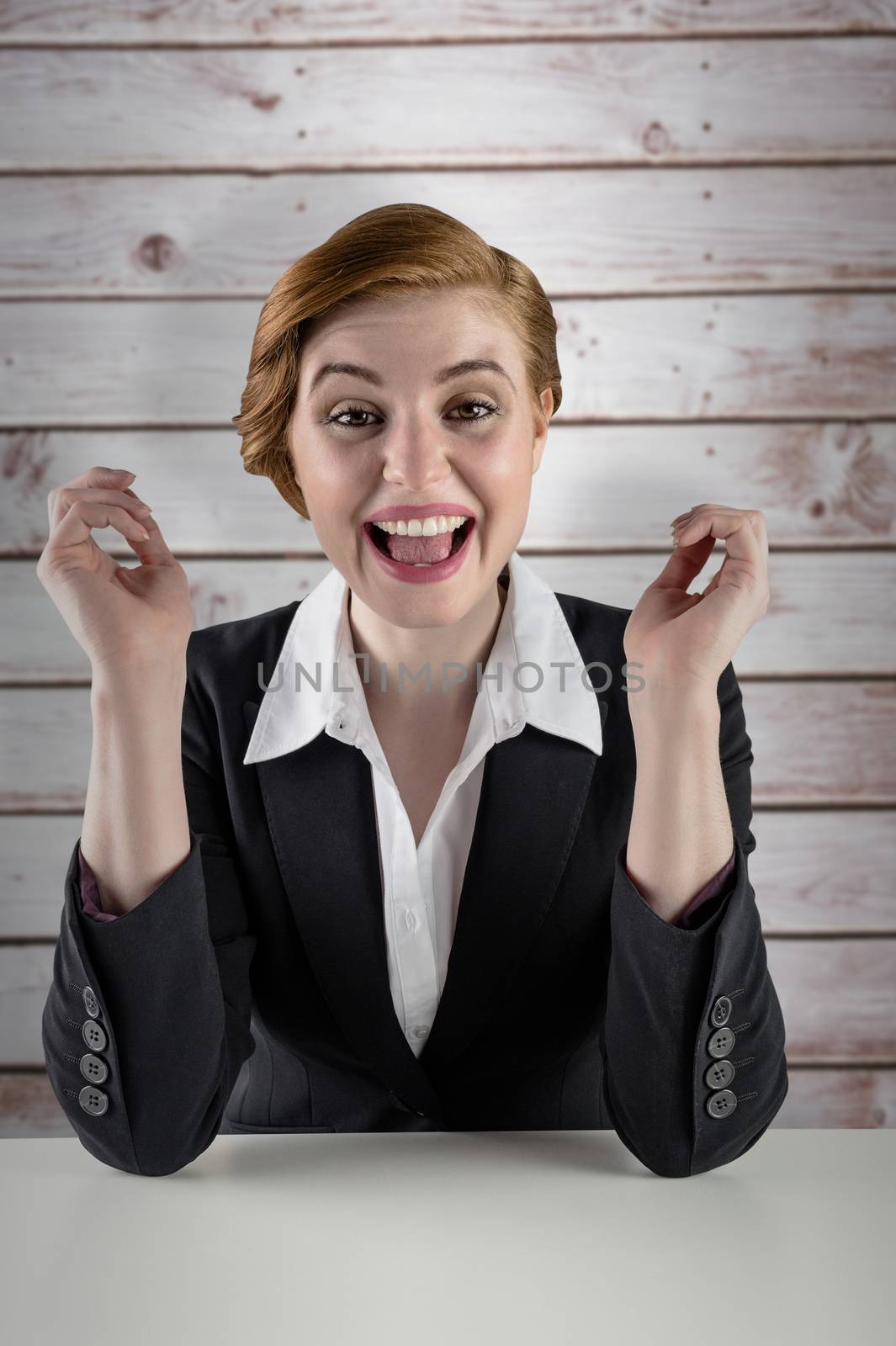 Composite image of excited redhead businesswoman sitting at desk by Wavebreakmedia