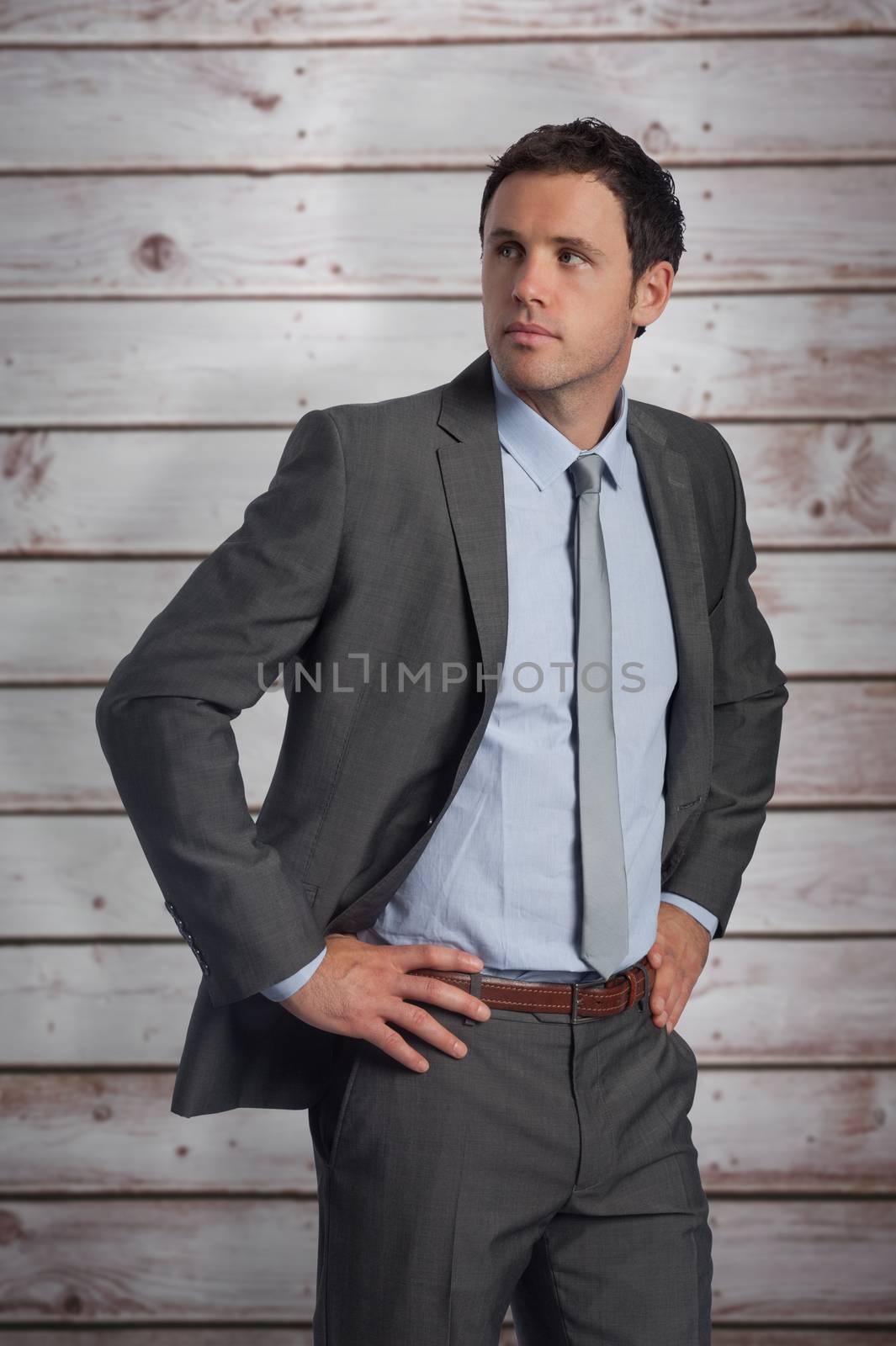 Serious businessman with hands on hips against wooden planks