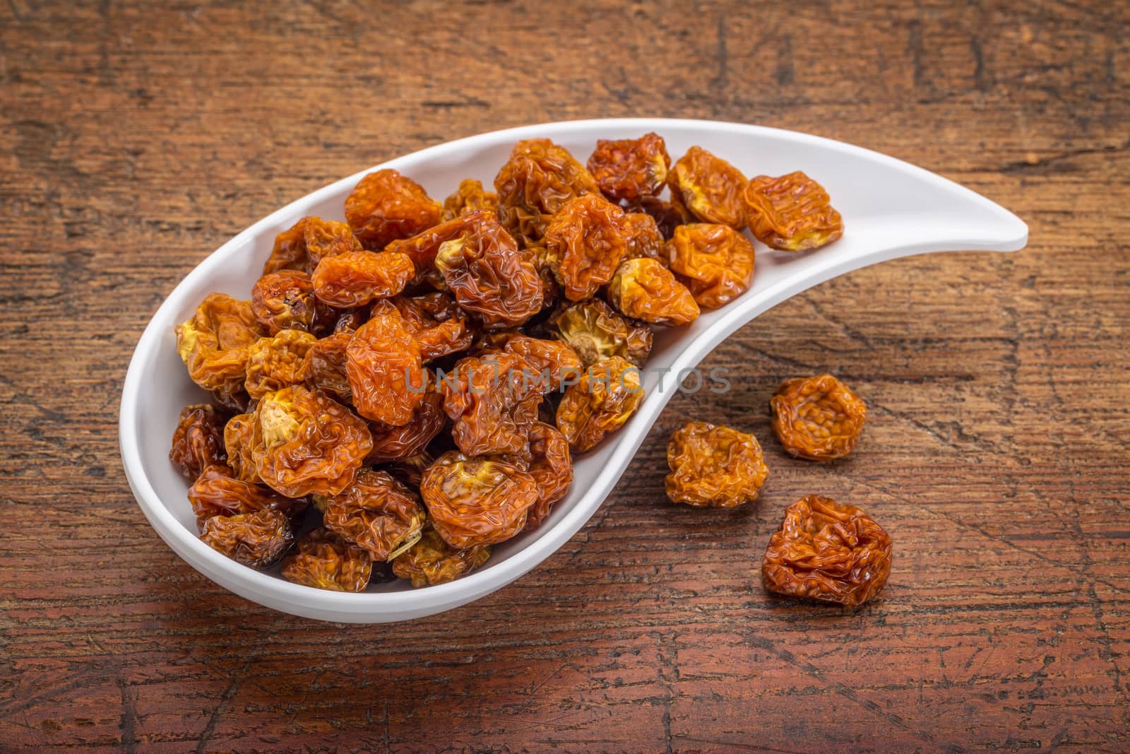 dried goldenberries in a ceramic teardrop shaped bowl against rustic scratched wood