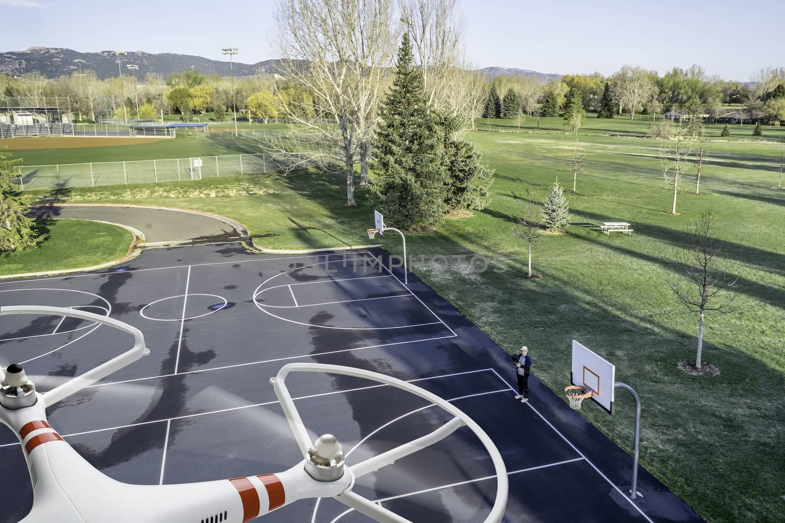quadcopter drone flying over empty basketball court with an operator standing