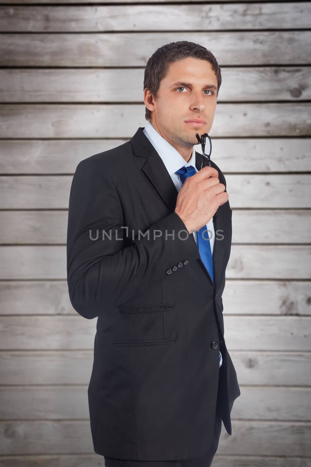 Thinking businessman holding glasses against wooden planks