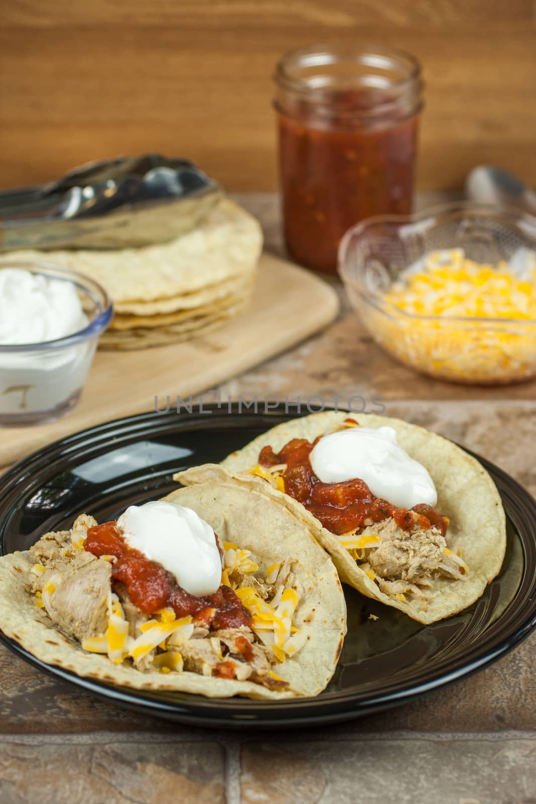 Pork carnitas with corn totillas on a dark plate with ingredients in the background.