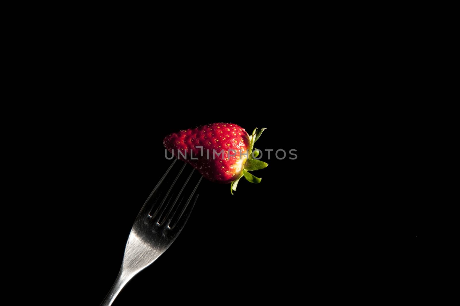 red strawberry on a fork with black background