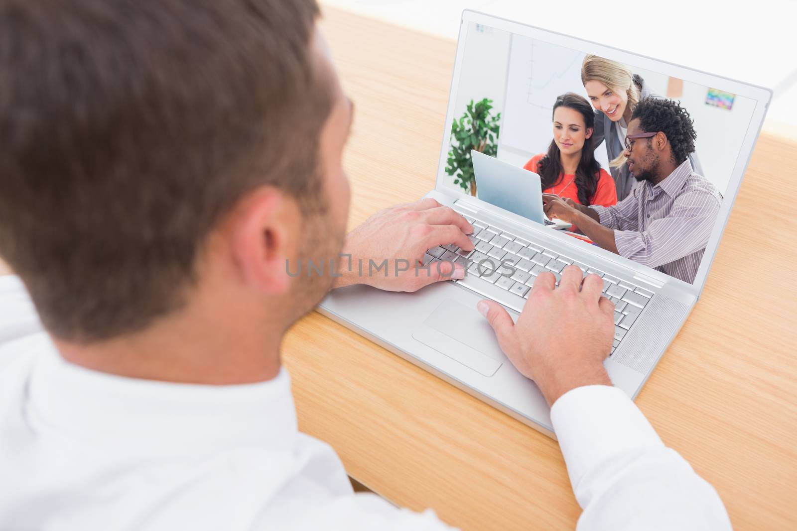 Three designers working together on a laptop against businessman working at his desk 