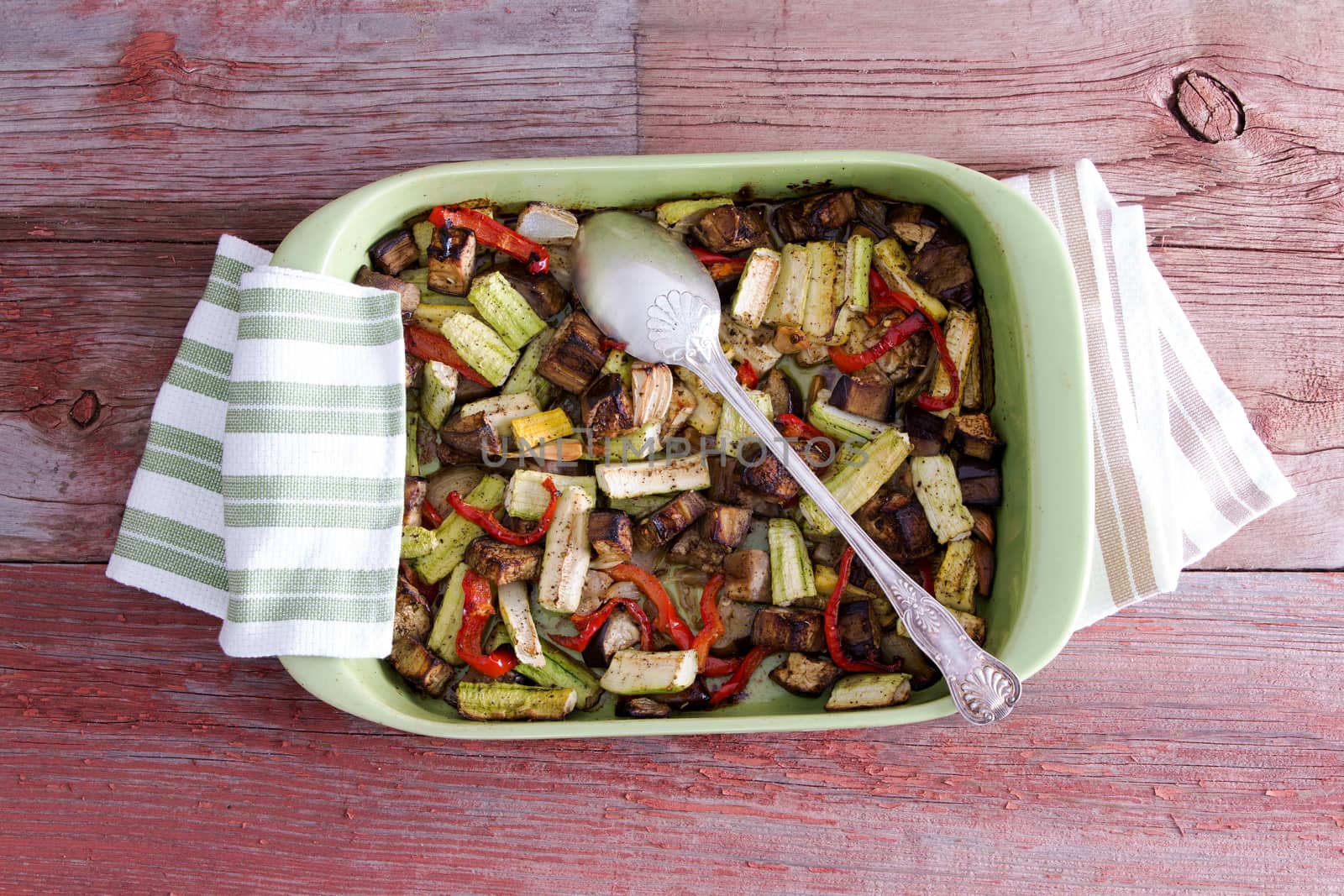 Delicious assorted fresh roast vegetables in an oven dish with kitchen cloth and serving spoon on a wooden table, high angle view