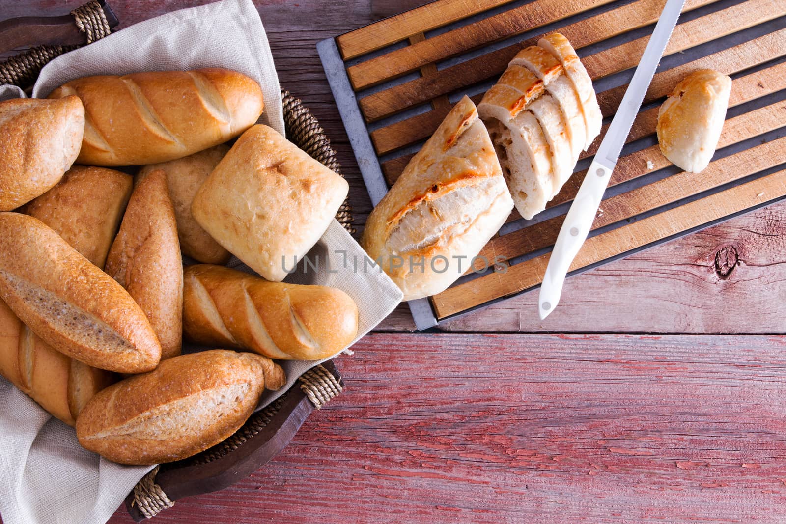 Sliced baguette and fresh crusty golden rolls in a wicker basket on a buffet table ready to be served as an accompaniment to dinner viewed from above on a wooden table with copyspace