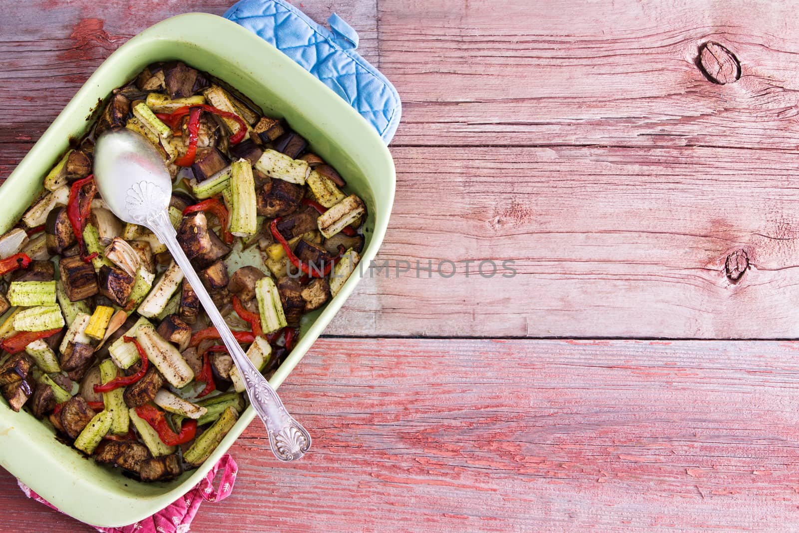 Baking dish filled with healthy roasted fresh vegetables for tasty vegetarian or vegan cuisine served on a rustic wooden table with copyspace, overhead view