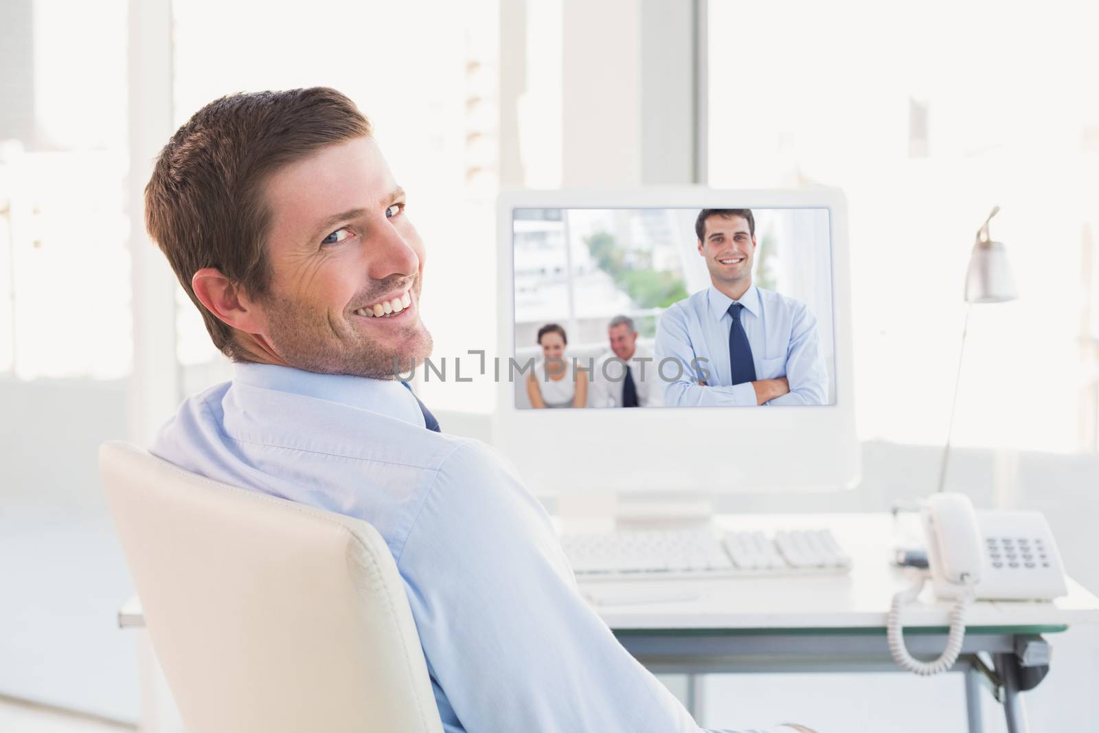 Cheerful businessman posing while his colleagues are working against smiling businessman sitting at his desk 