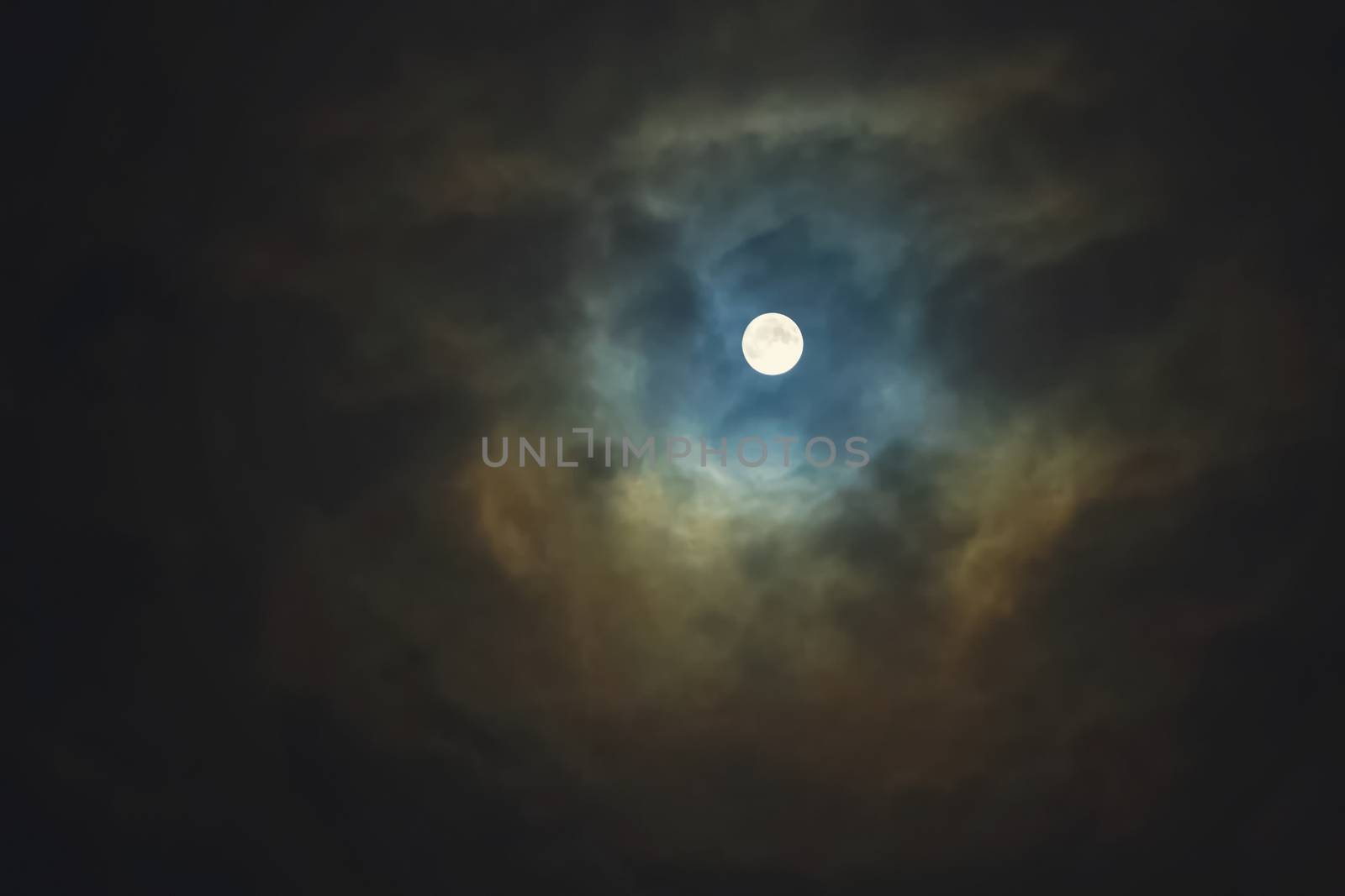 Full moon shines through dramatic sky surrounded clouds