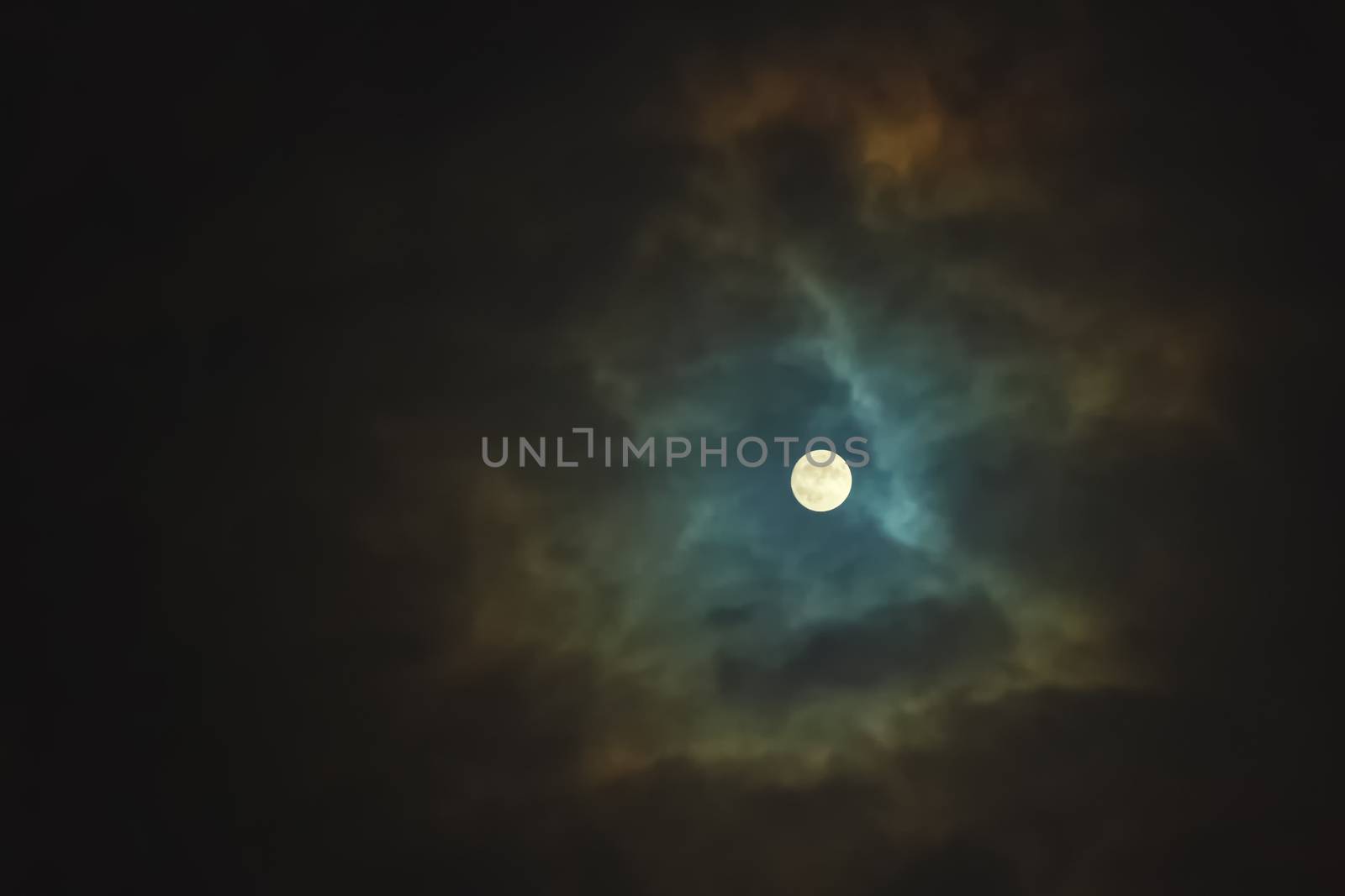 Full moon shines through dramatic sky surrounded clouds