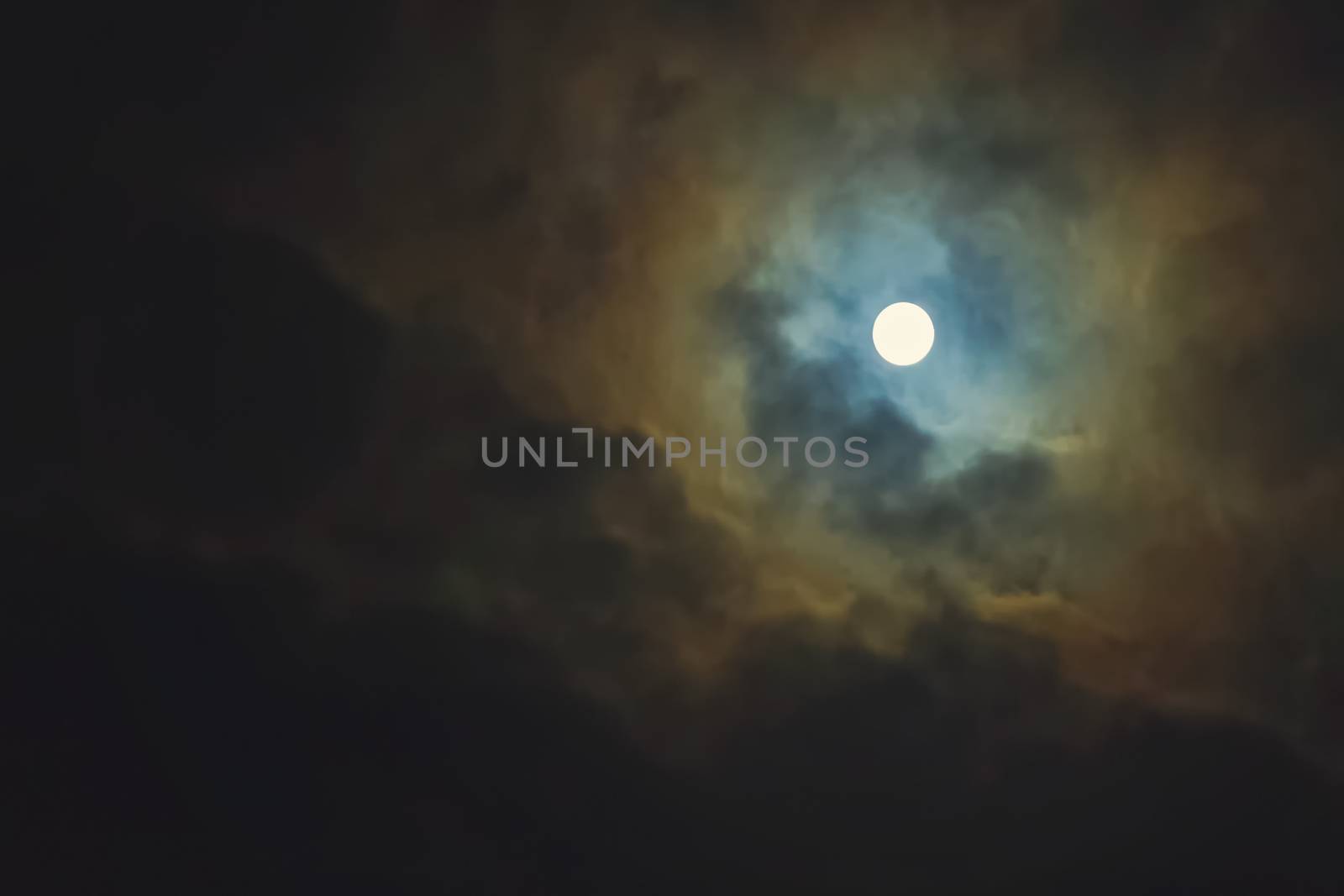 Full moon shines through dramatic sky surrounded clouds