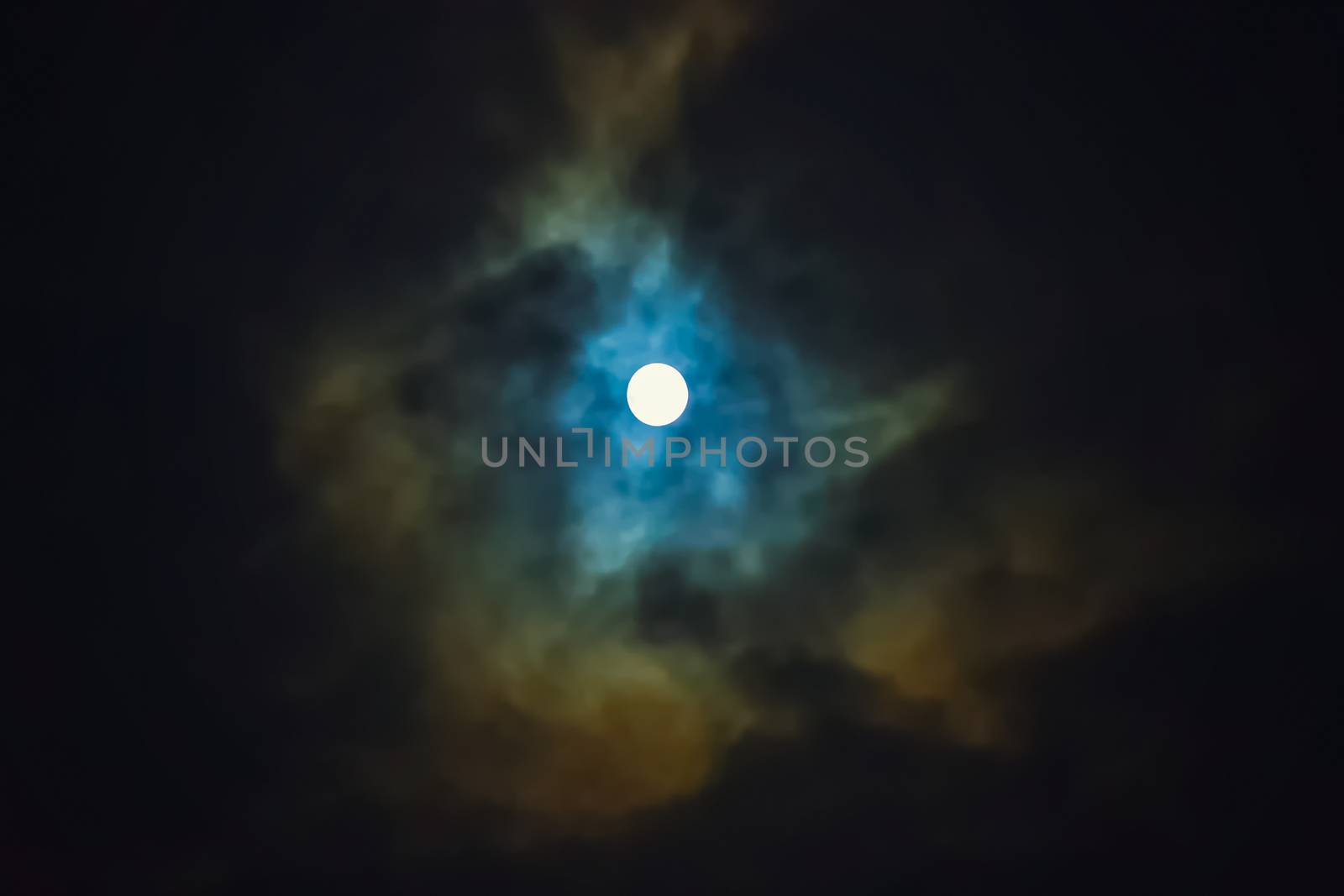 Full moon shines through dramatic sky surrounded clouds