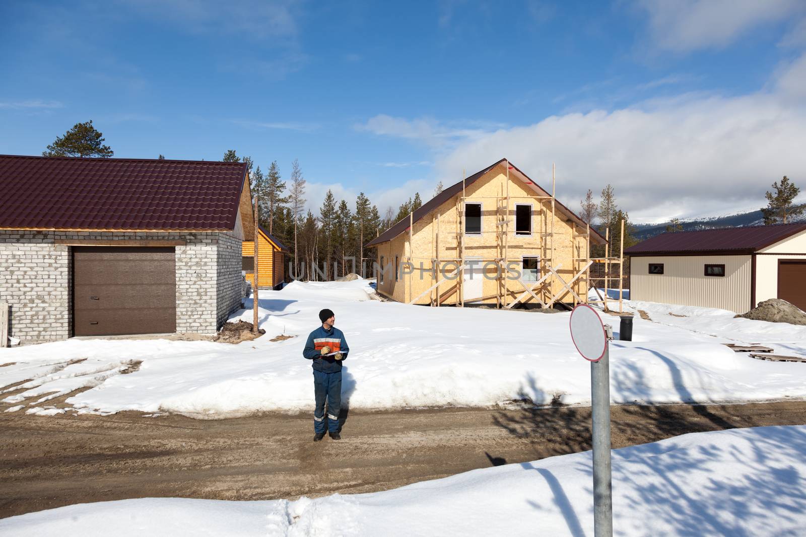 Worker in overalls making notes on construction site by AleksandrN