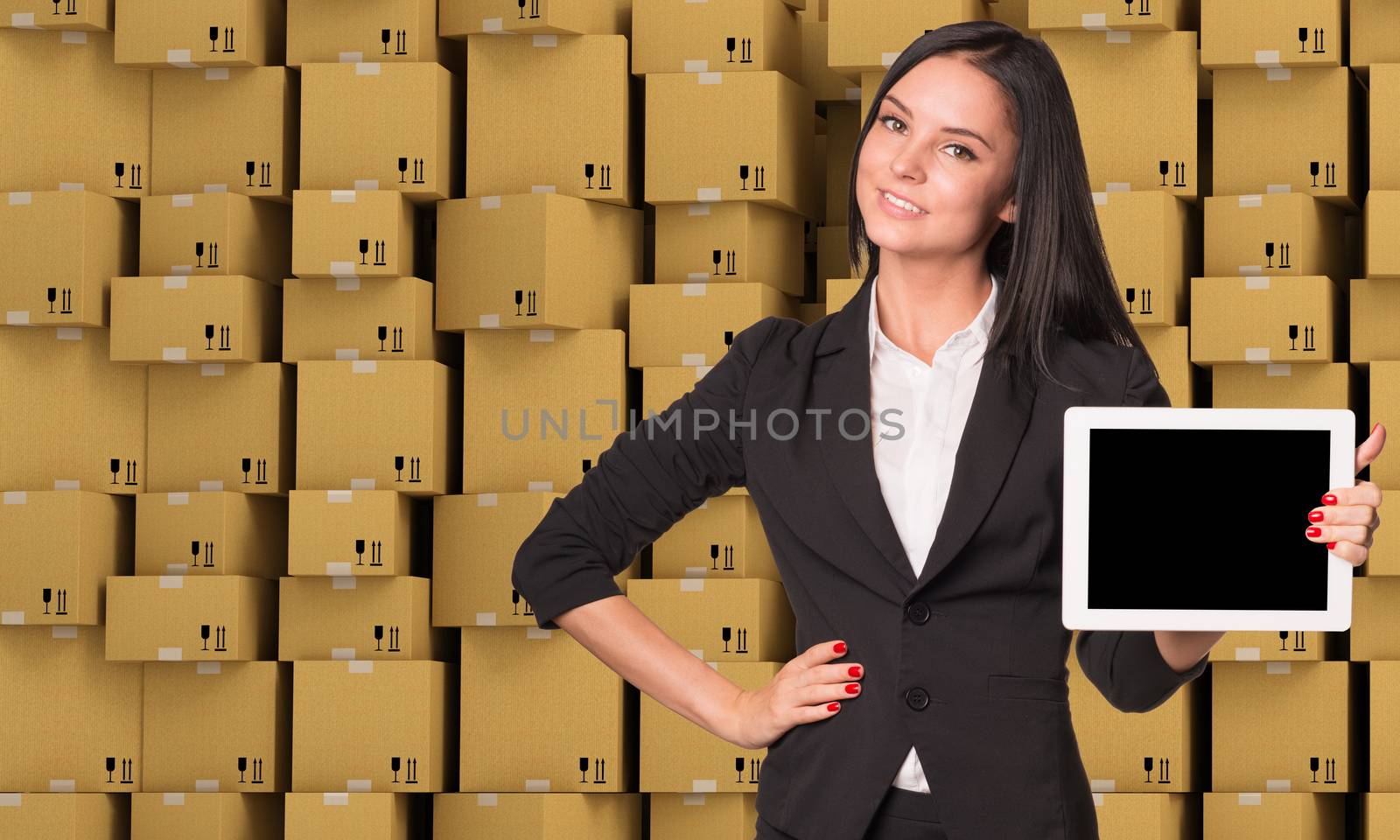Smiling young woman holging tablet and looking at camera on abstract cardboard boxes set  background
