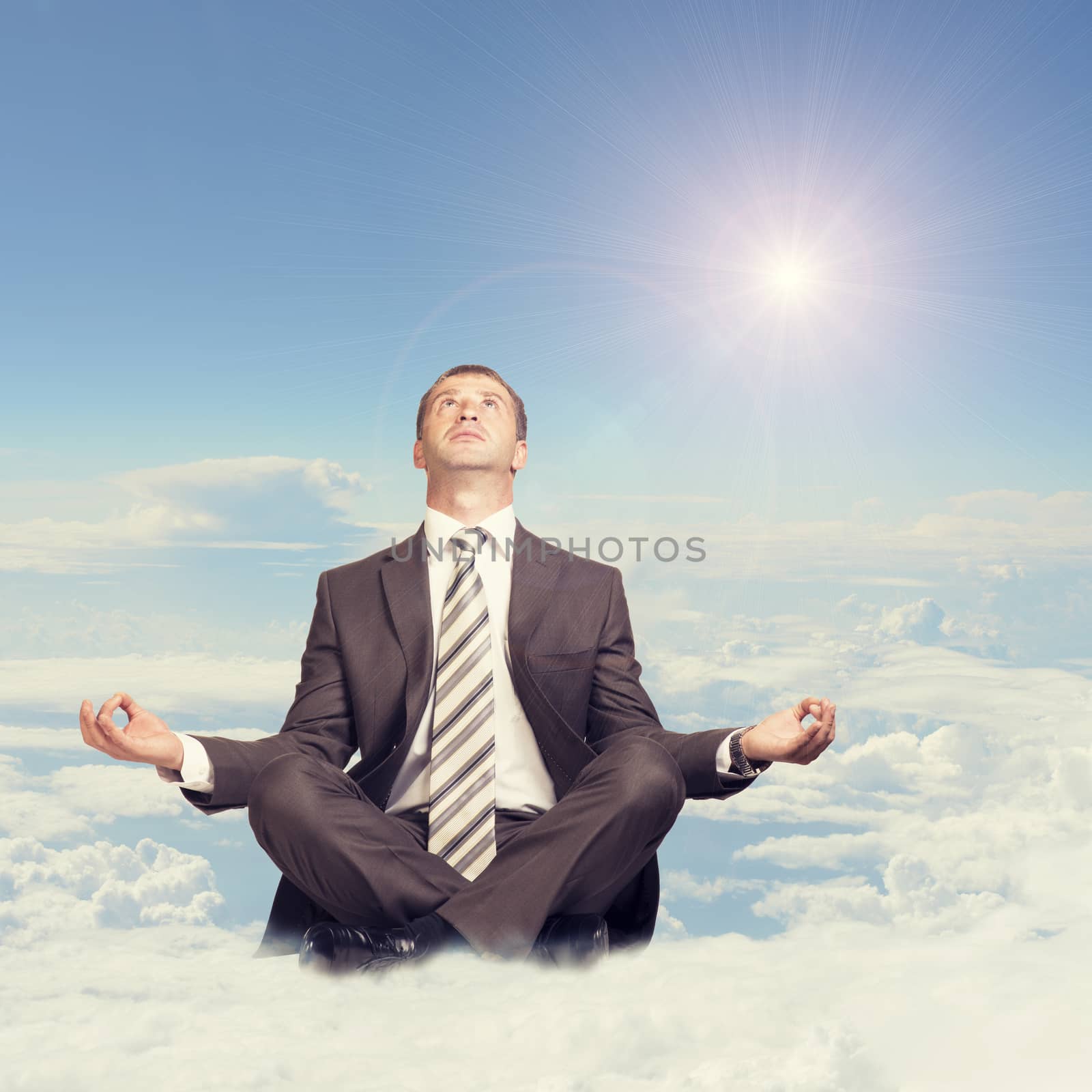 Businessman sitting in lotus position on cloud and looking up