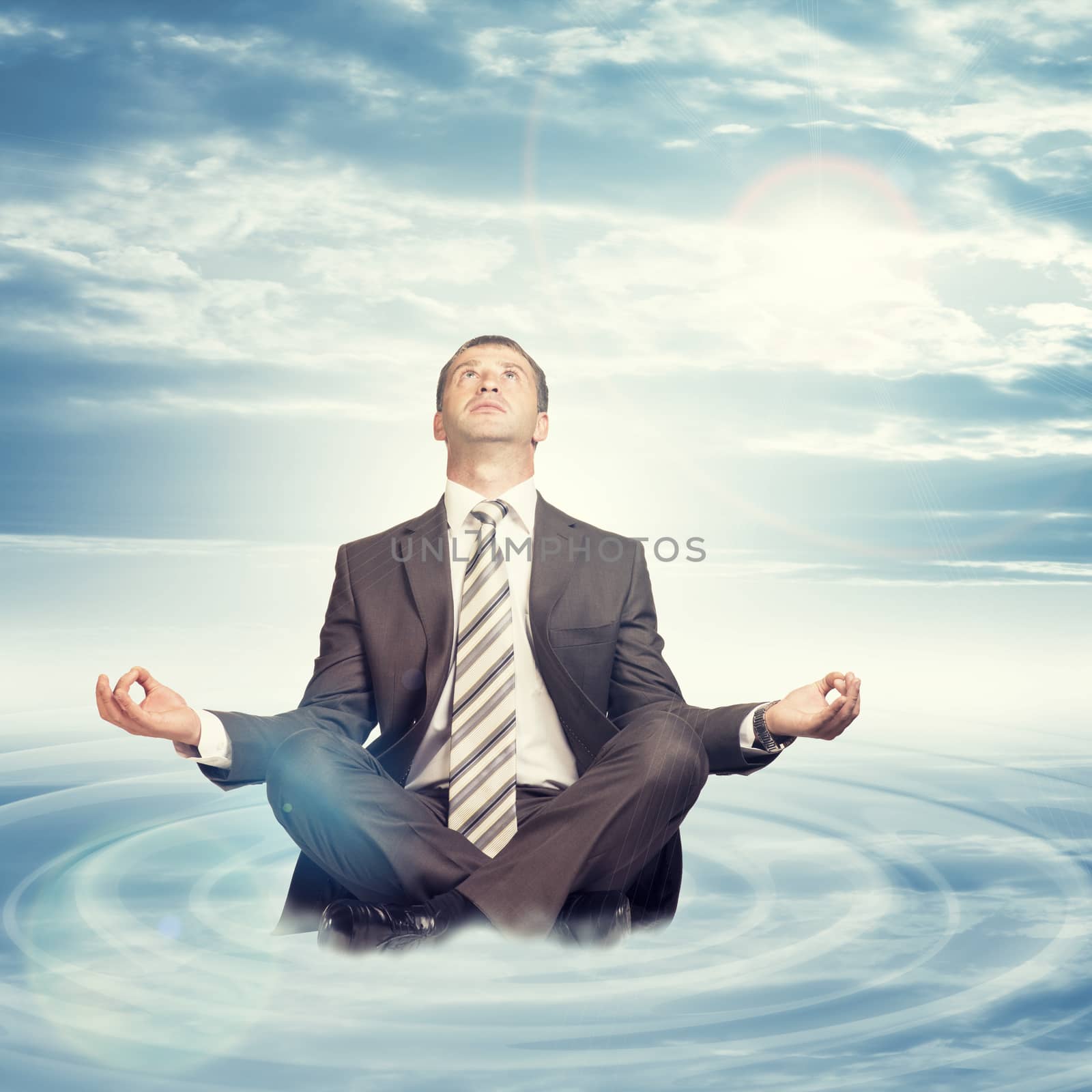 Businessman sitting in lotus position on cloud with circles and looking up on blue sky background