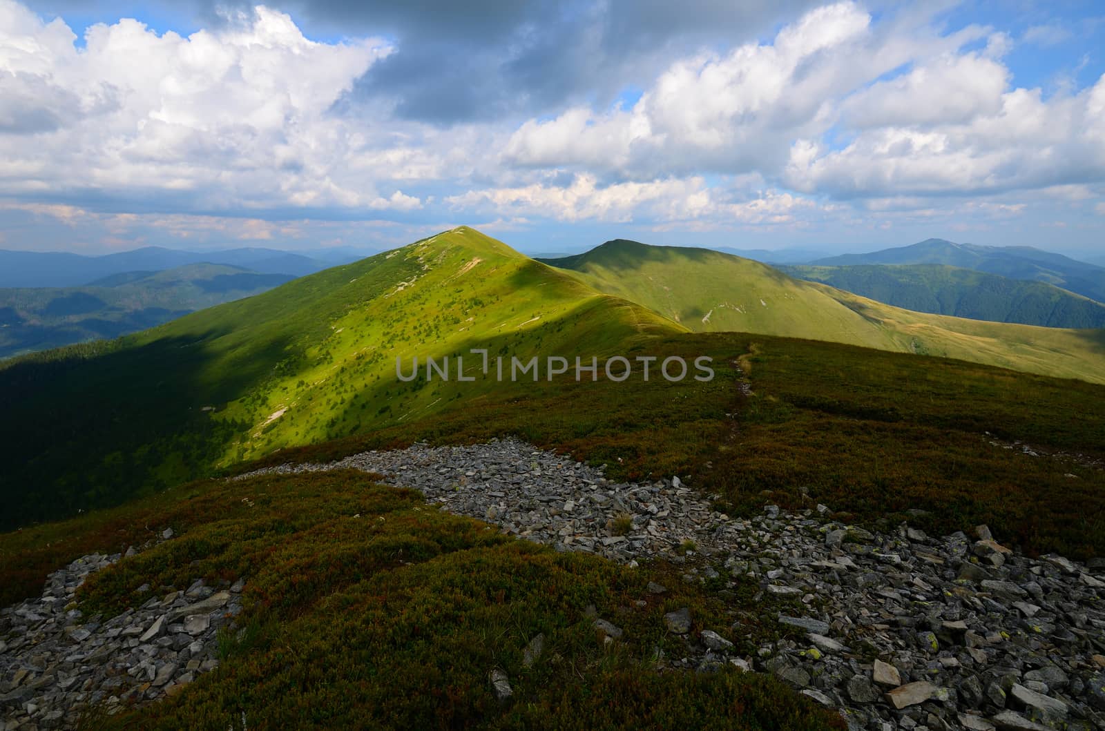 Mountain range with green grassy hills and light patches and rocks on the foreground