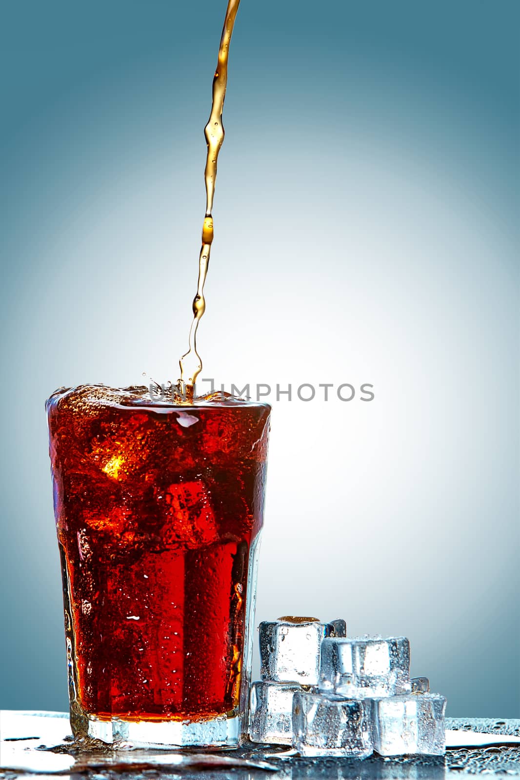 Cola pouring in a glass  with ice on a blue background