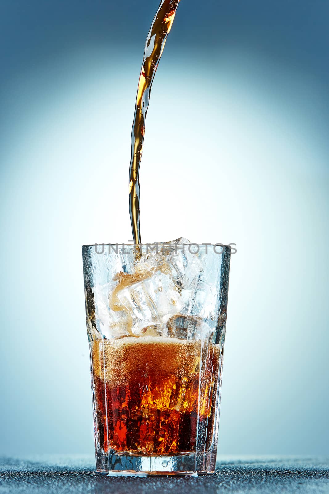 Cola pouring in a glass  with ice on a blue background