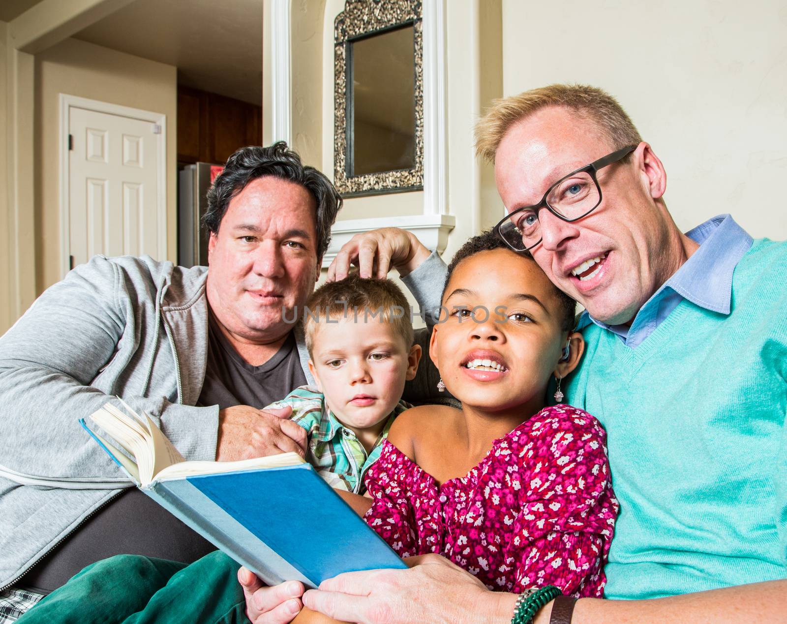 An attractive gay couple reads to their children in living room