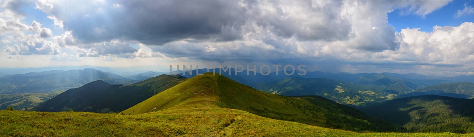 Panoramic mountains landscape with grassy range and cloudy sky and sun rays