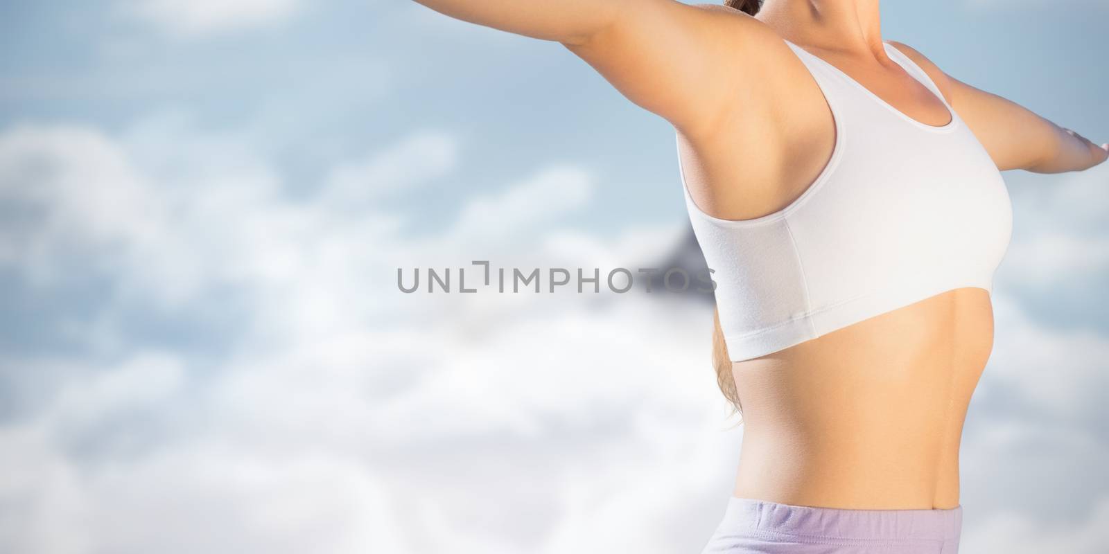 Sporty blonde standing on the beach with arms out against mountain peak through the clouds