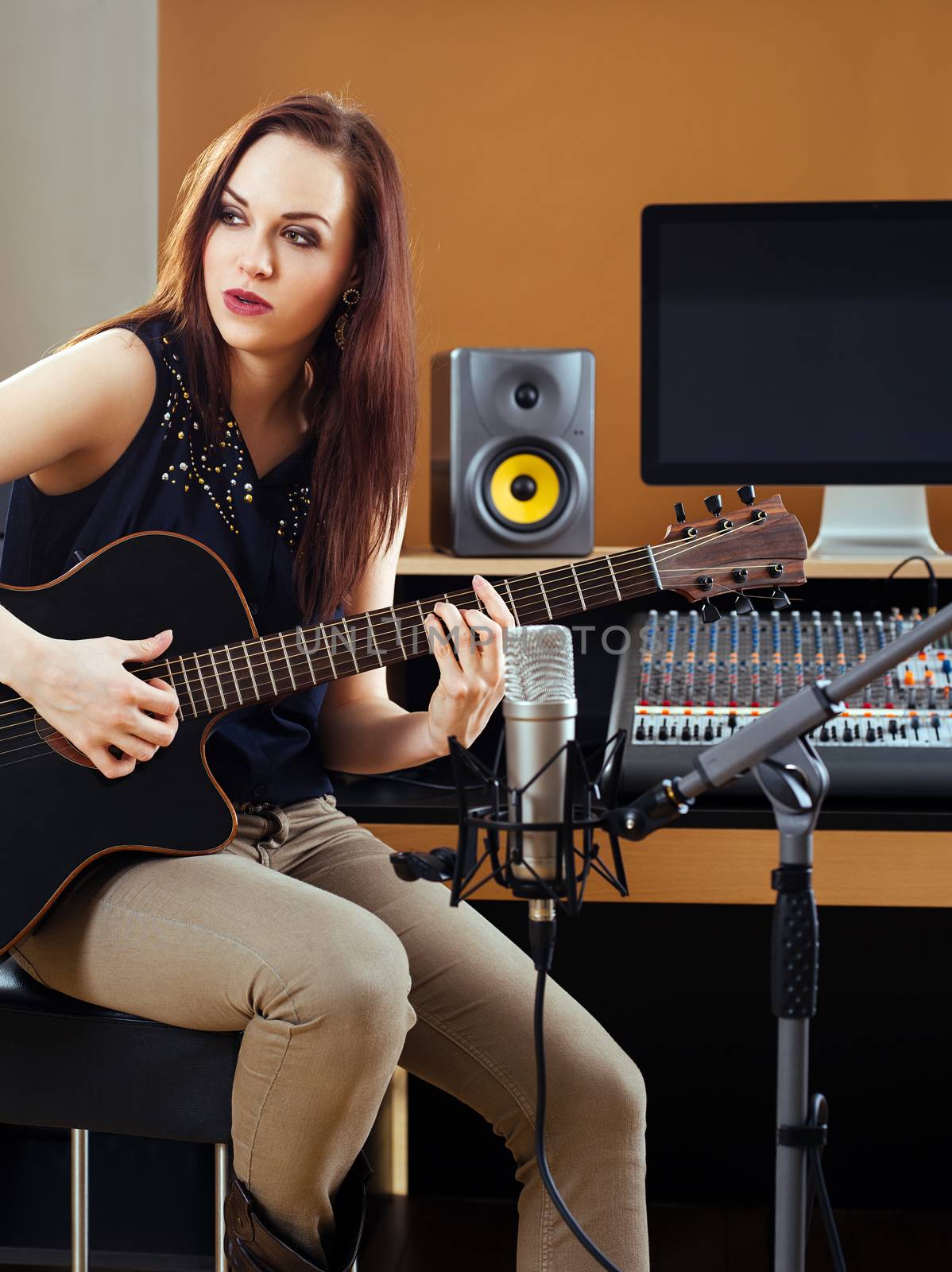 Photo of a beautiful brunette in a recording studio recording her guitar tracks.
