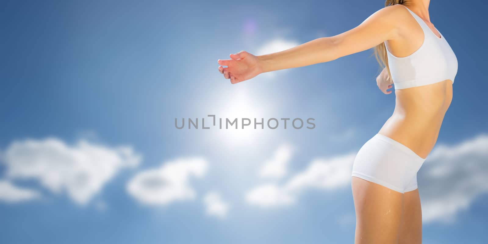 Gorgeous fit blonde standing with arms out against cloudy sky with sunshine