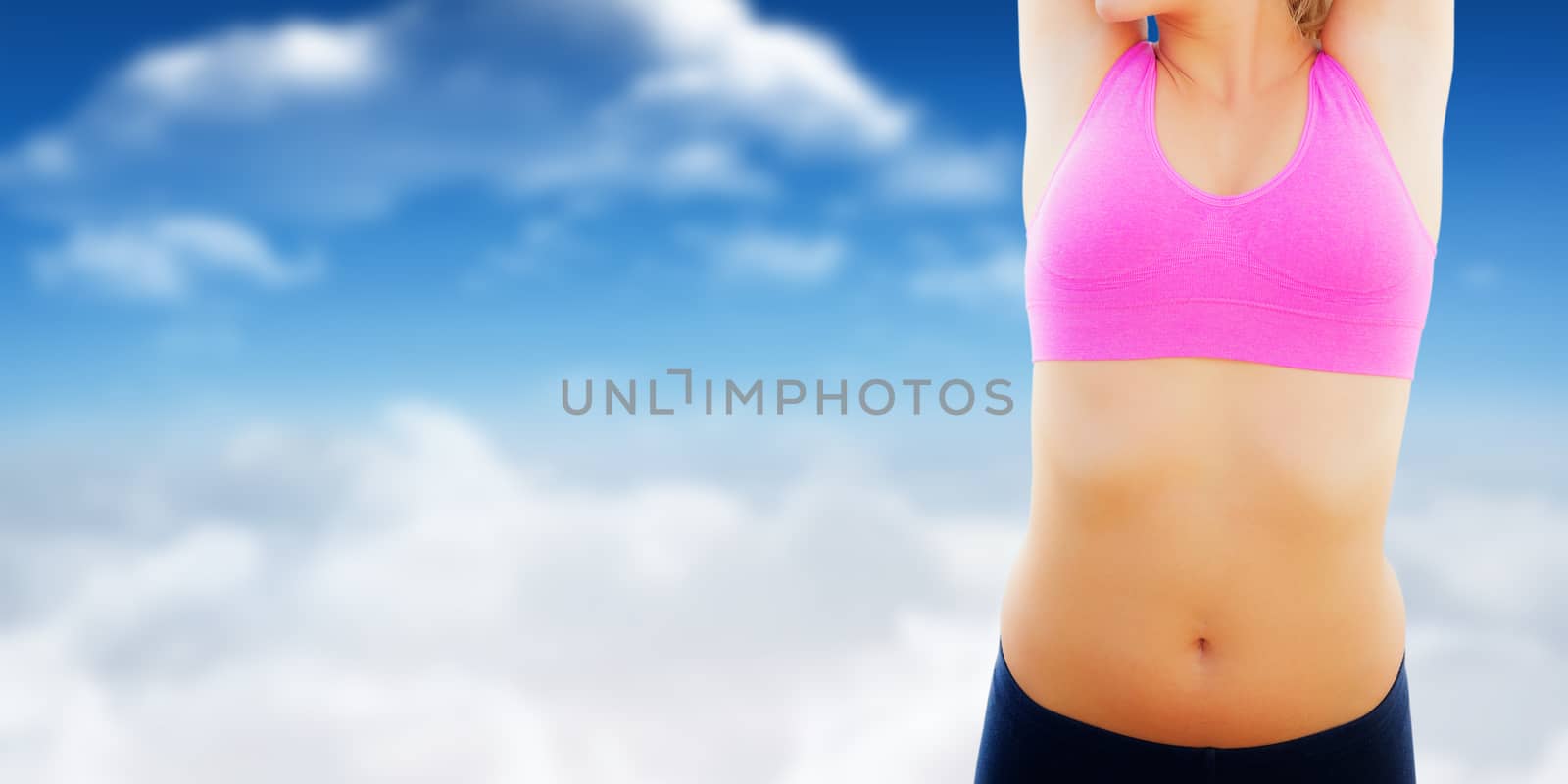 Smiling toned woman stretching hands on beach against bright blue sky with clouds