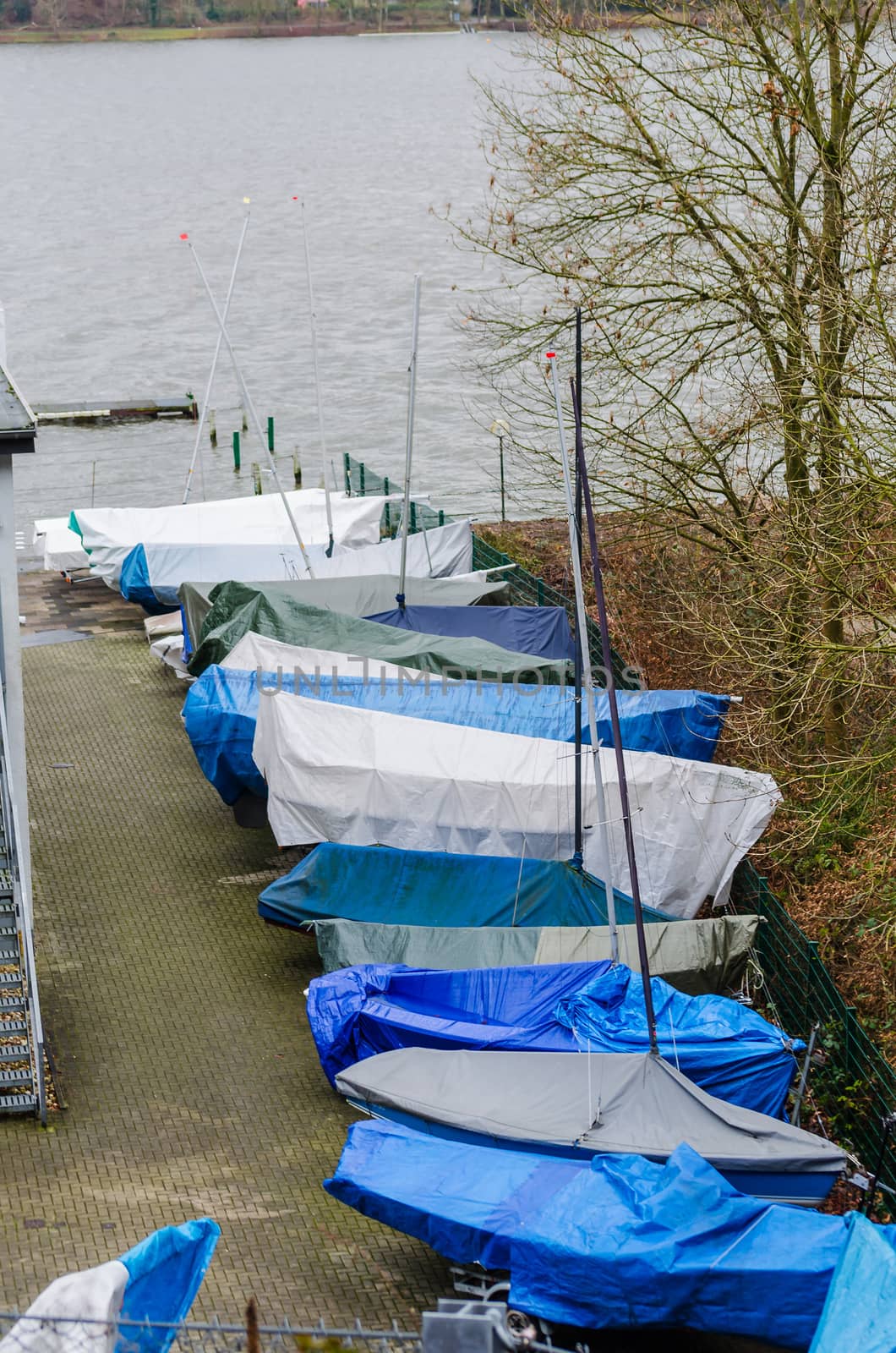 Small sailboats covered with a blue tarp for the winter on land.