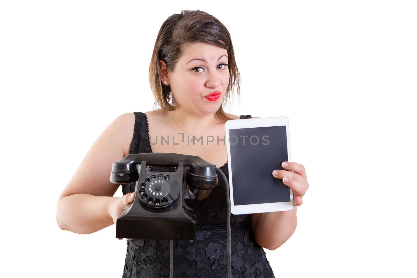 Charismatic woman comparing old and modern technology holding up an old-fashioned rotary land line telephone instrument and a tablet computer in a communications concept, isolated on white